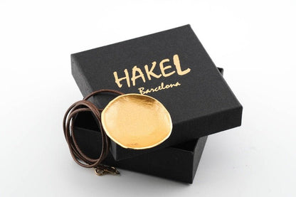 Gold-tone round pendant necklace with brown cords, shown with black gift box