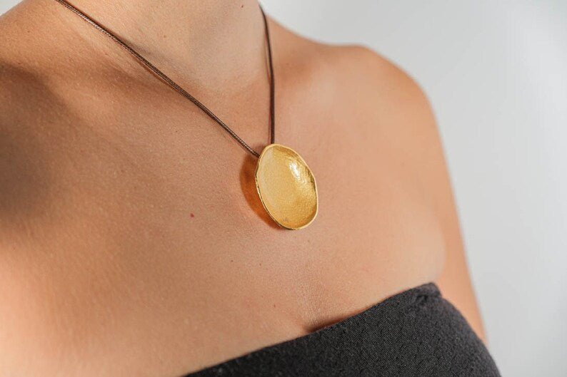 Gold-tone round pendant necklace on a cord, worn at neckline