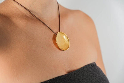 Gold-tone round pendant necklace on a cord, worn at neckline