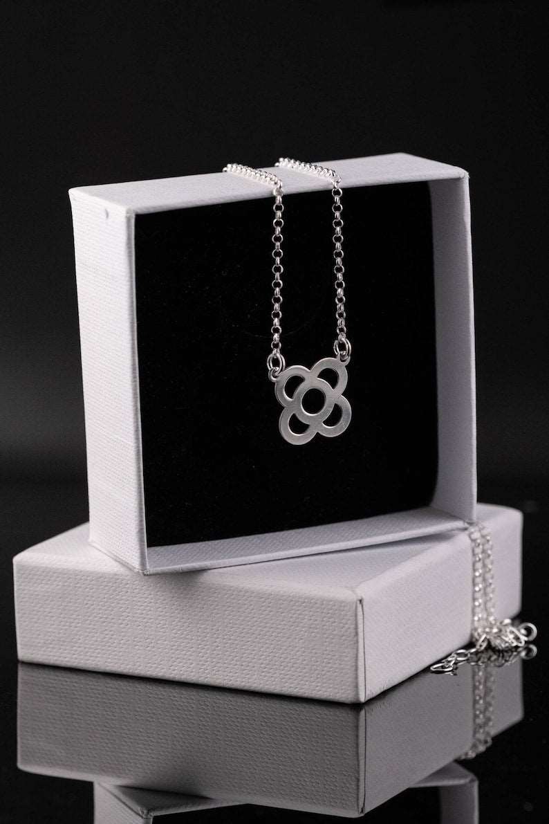 Silver flower pendant necklace displayed on a white jewelry box with chain.