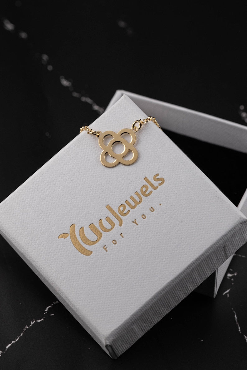 Gold flower pendant necklace on a white jewelry box with petal-shaped charm.