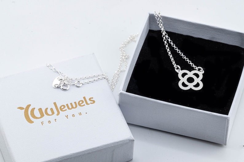 Silver flower pendant necklace resting in a white jewelry box with link chain.