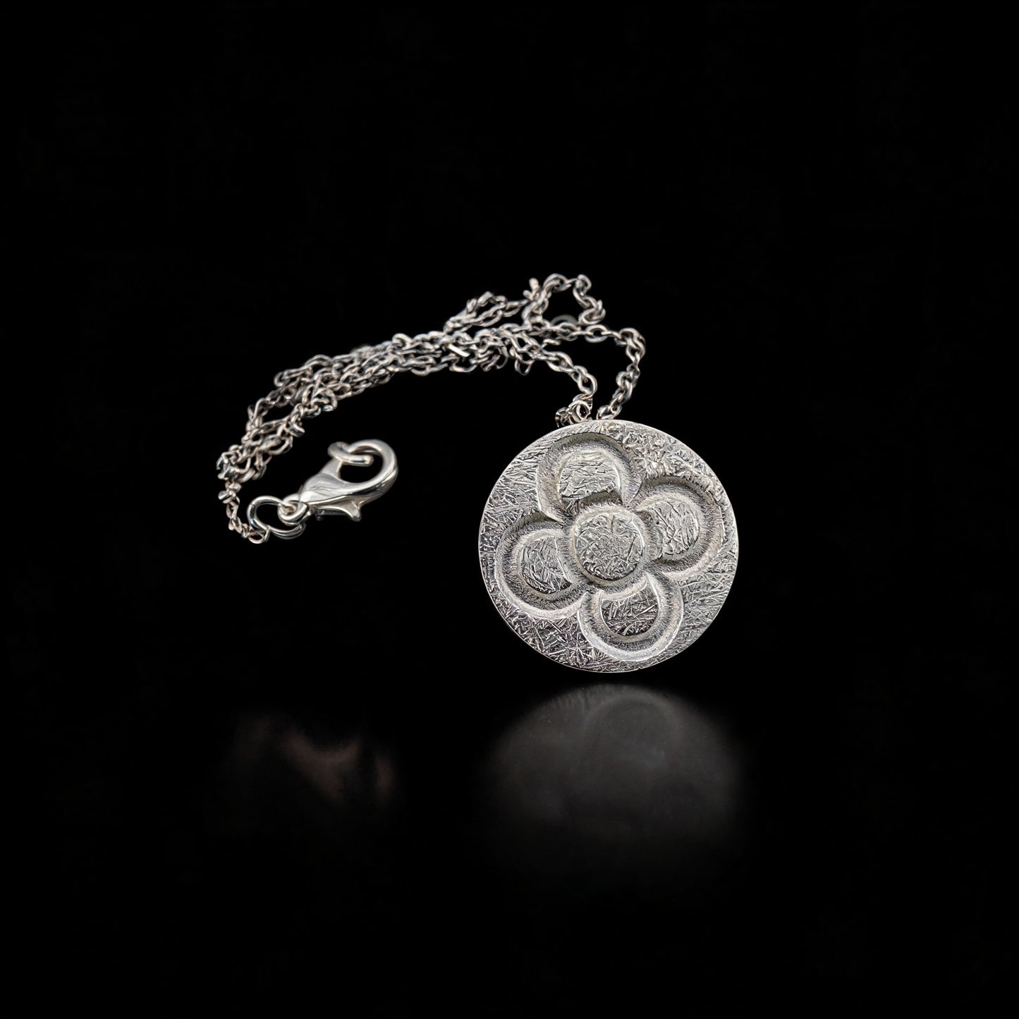 Round silver flower pendant with chain and clasp, circular textured design