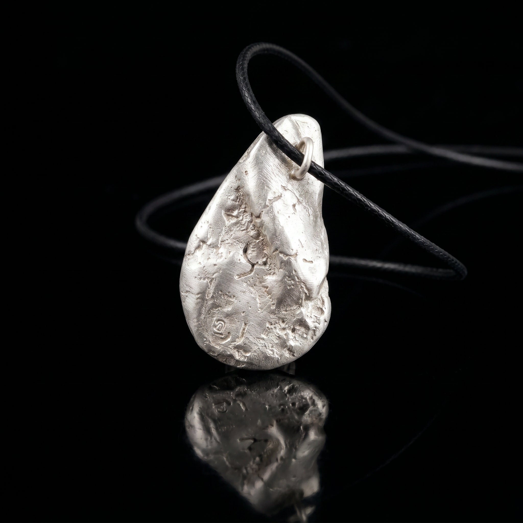 Silver-tone hammered teardrop pendant on black cord with metal loop