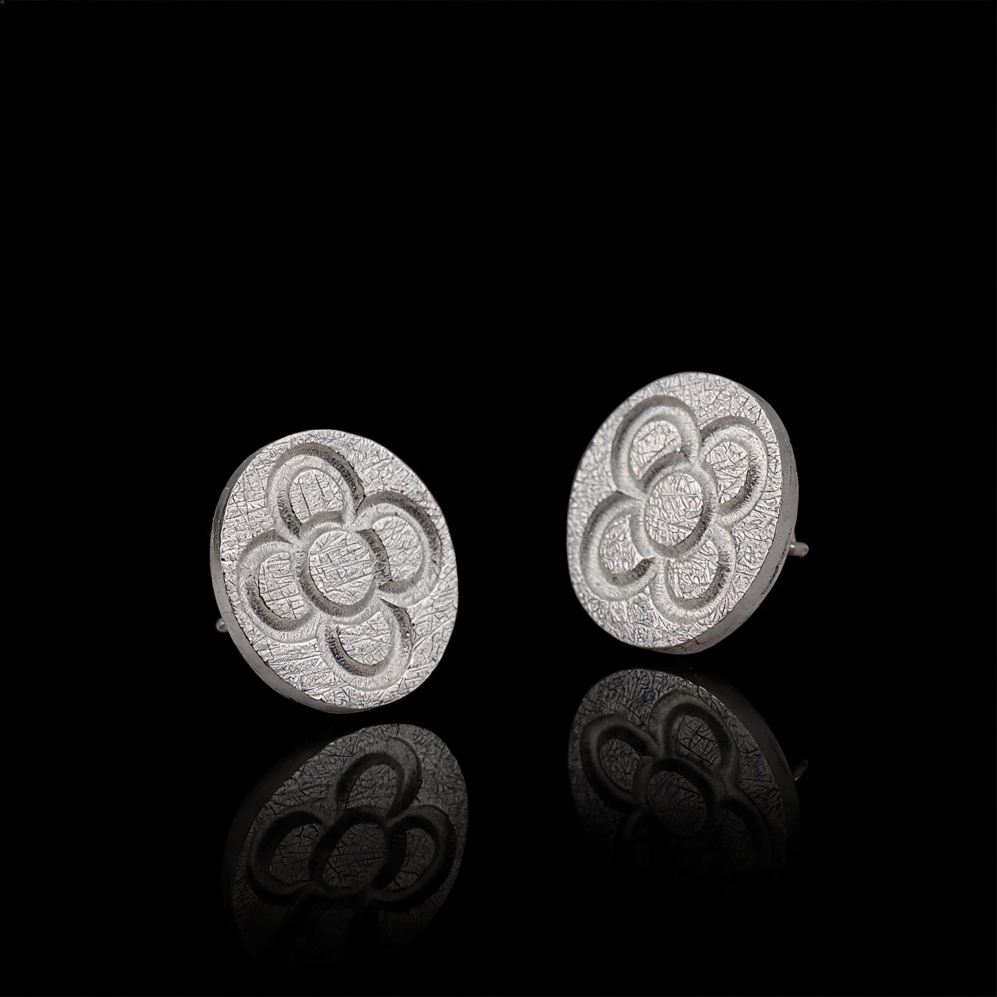 Silver round stud earrings with raised four-petal flower pattern and post backs