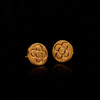 Pendientes redondos de oro con patrón de flor en relieve sobre fondo oscuro reflectante