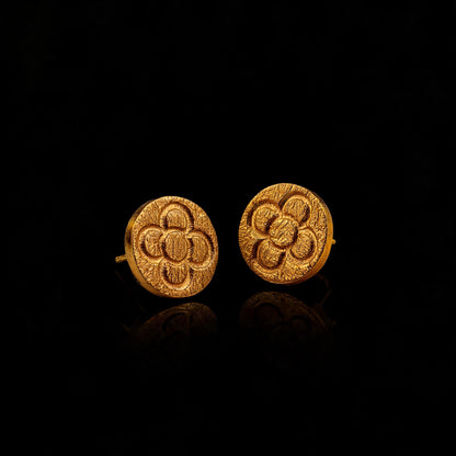 Gold round stud earrings with raised flower pattern on dark reflective background