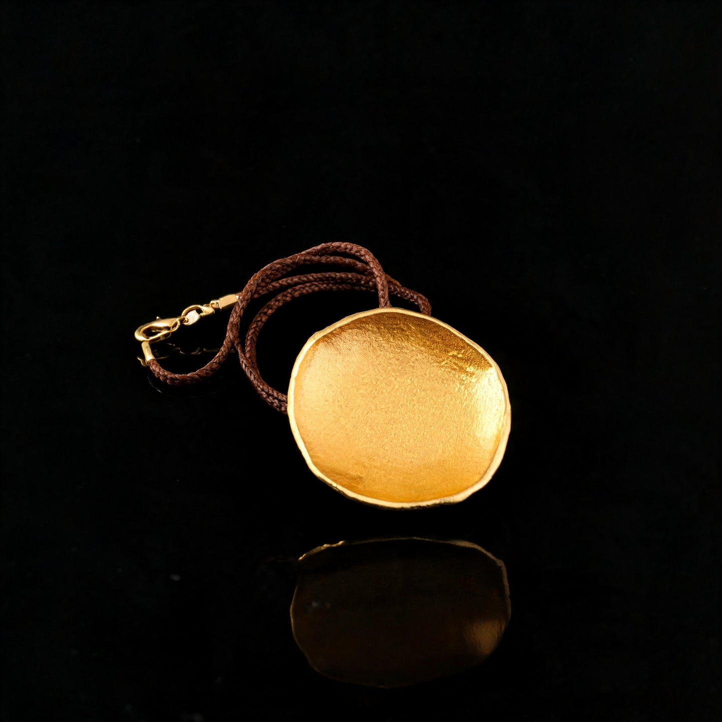 Gold-tone round pendant necklace with brown braided cord and chain loop