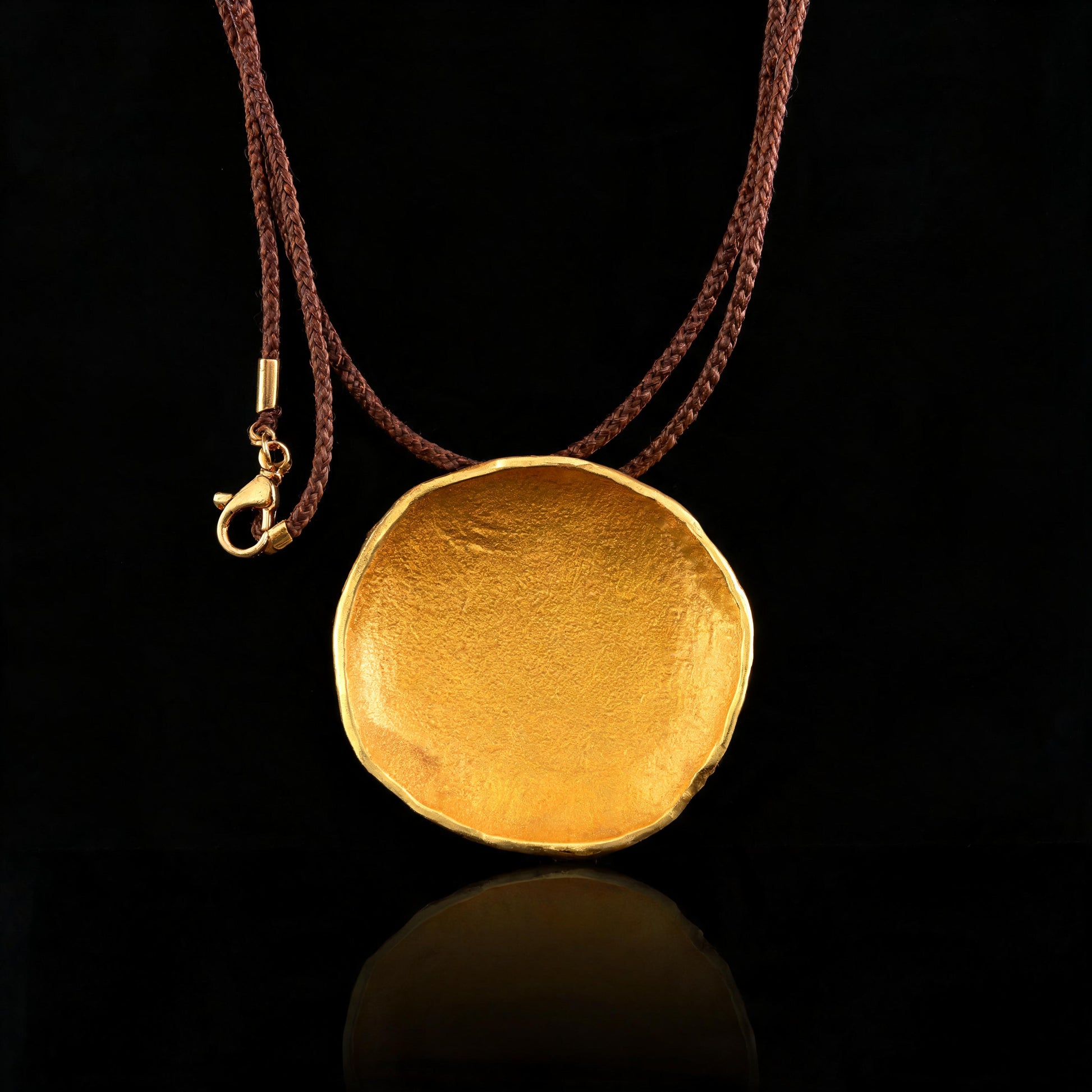 Gold-tone round pendant necklace on brown cord, lobster clasp visible