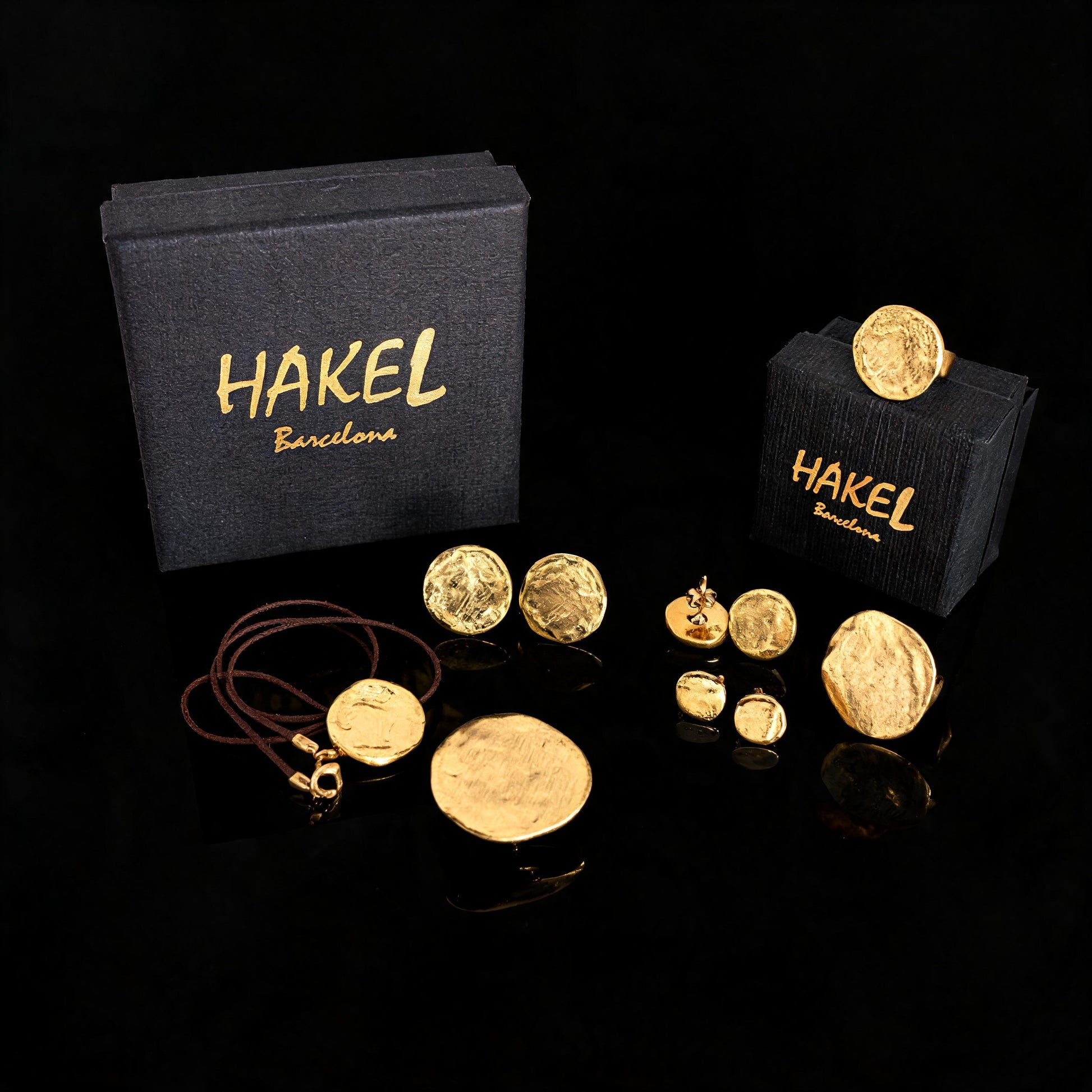 Gold stud and drop earrings set with small round discs, shown with HAKEL boxes