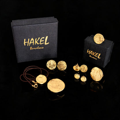 Gold stud and drop earrings set with small round discs, shown with HAKEL boxes
