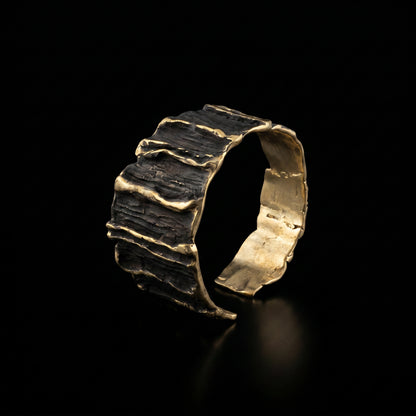 Sculpted gold-tone cuff bracelet with dark ridged bands and gold-highlighted edges
