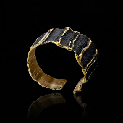 Sculpted gold-tone cuff bracelet with dark ridged panels and raised gold accents